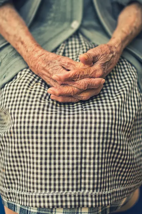 Older woman's hands on gingham apron