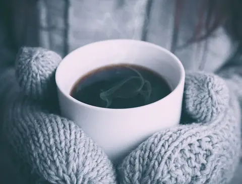 Mug of coffee held in knitted mittens
