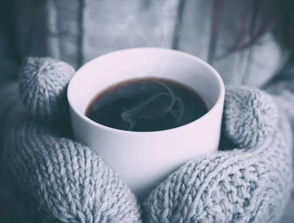 Mug of coffee held in knitted mittens