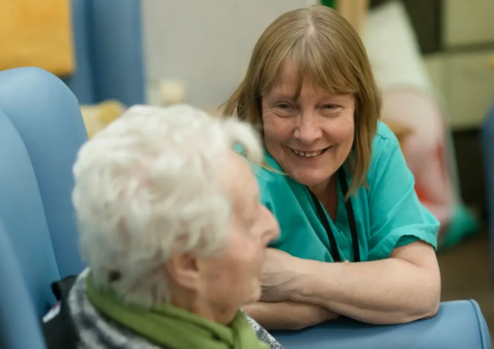 Carer in teal tunic smiling with older woman