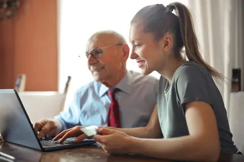 Young woman helping older man in shirt and tie at a laptop
