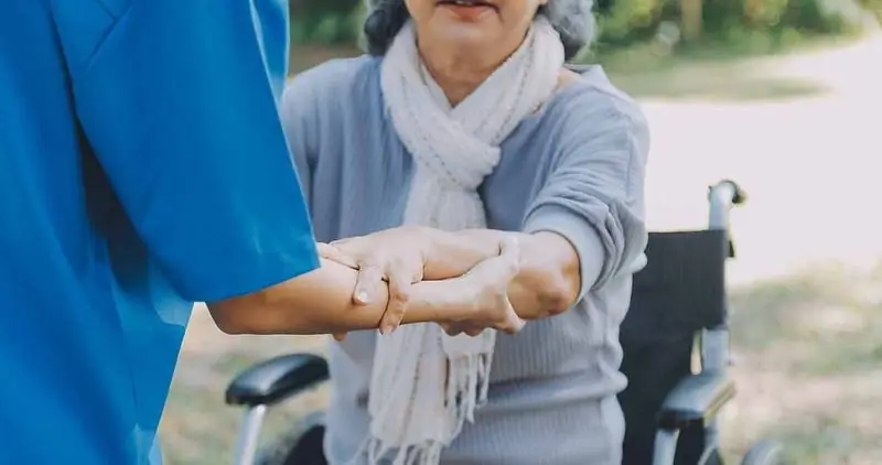 A carer supporting an older woman's arm beside her wheelchair