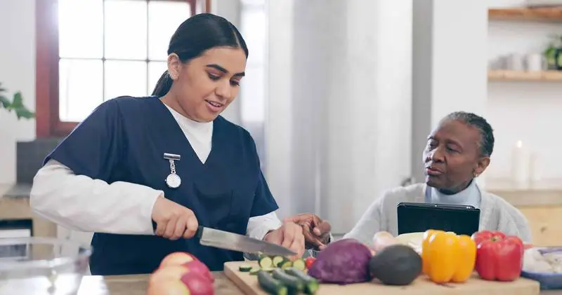 Carer and client preparing vegetables together in a kitchen