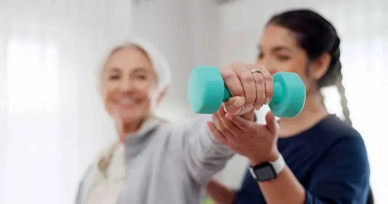 A carer helping an older woman with a light hand weight