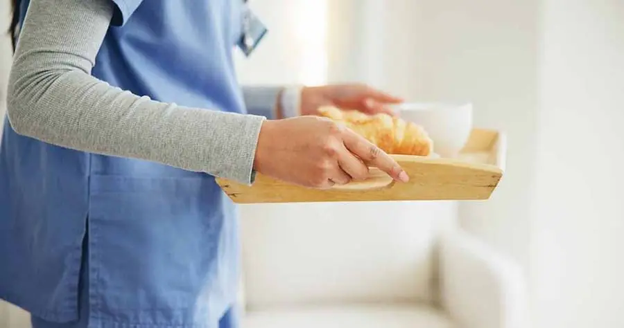 A carer carrying a breakfast tray into a living room